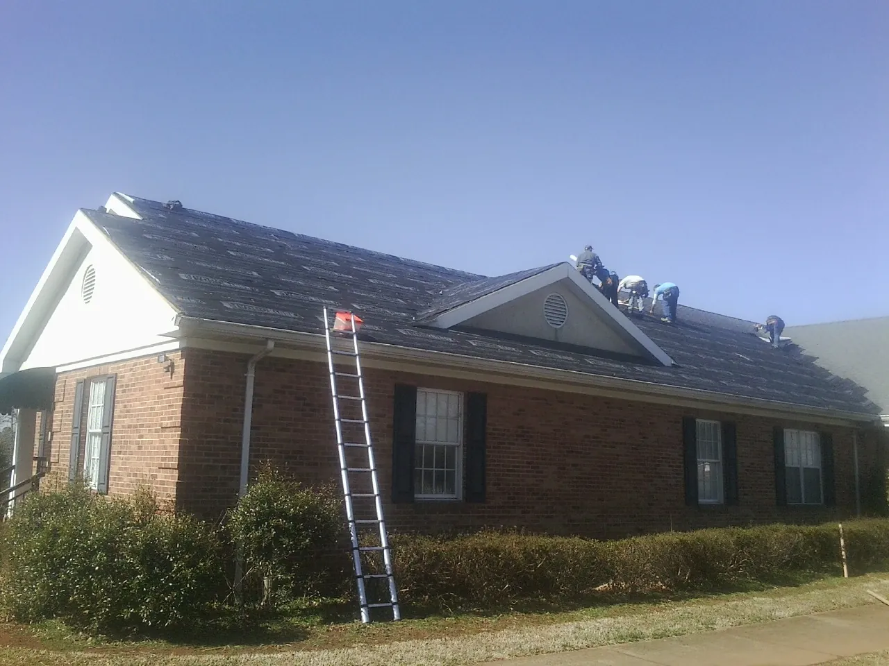 Crew tearing shingles off a brick ranch roof with a ladder set — Metal Roof Repair work by our crew in Burley