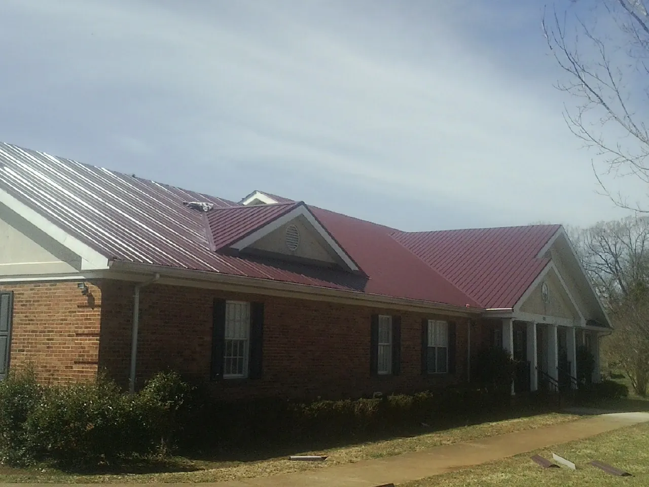 Red metal roof with gabled entries on a long brick building, from a Hail Damage Roof Repair job in Burley