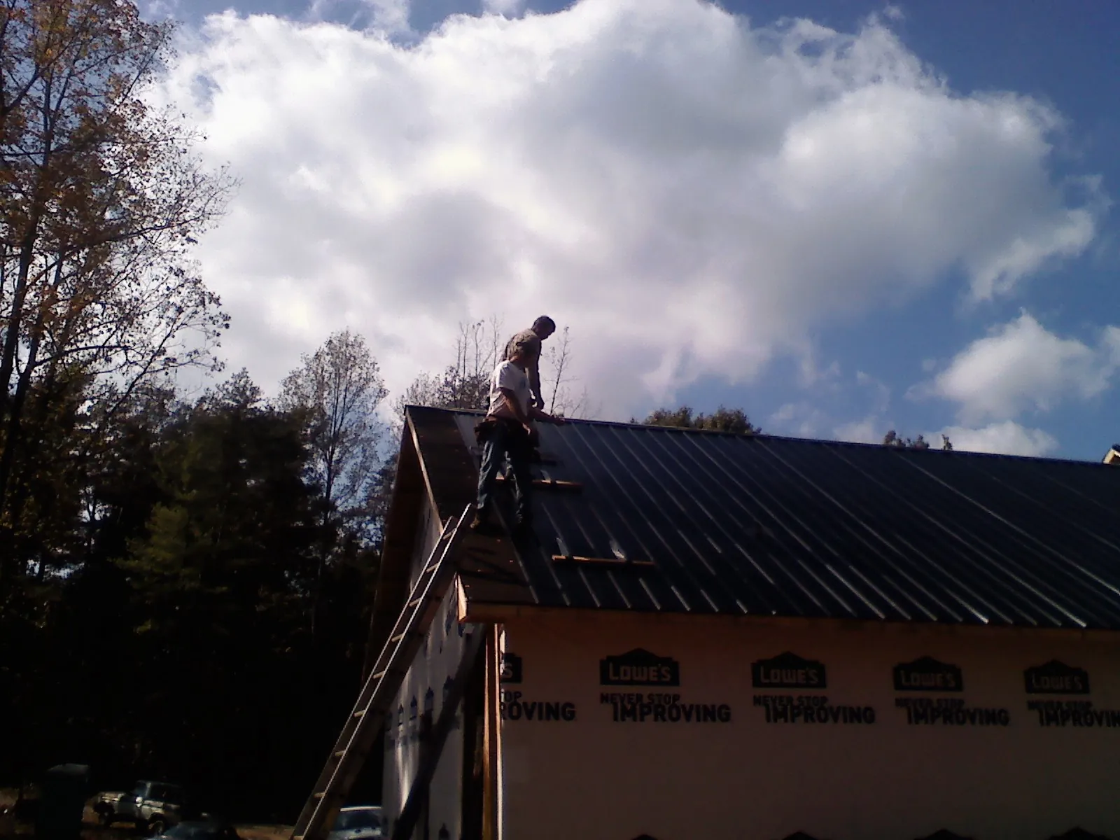 Roofer fastening dark metal panels high against a cloudy sky, from a Roof Inspection job in Burley