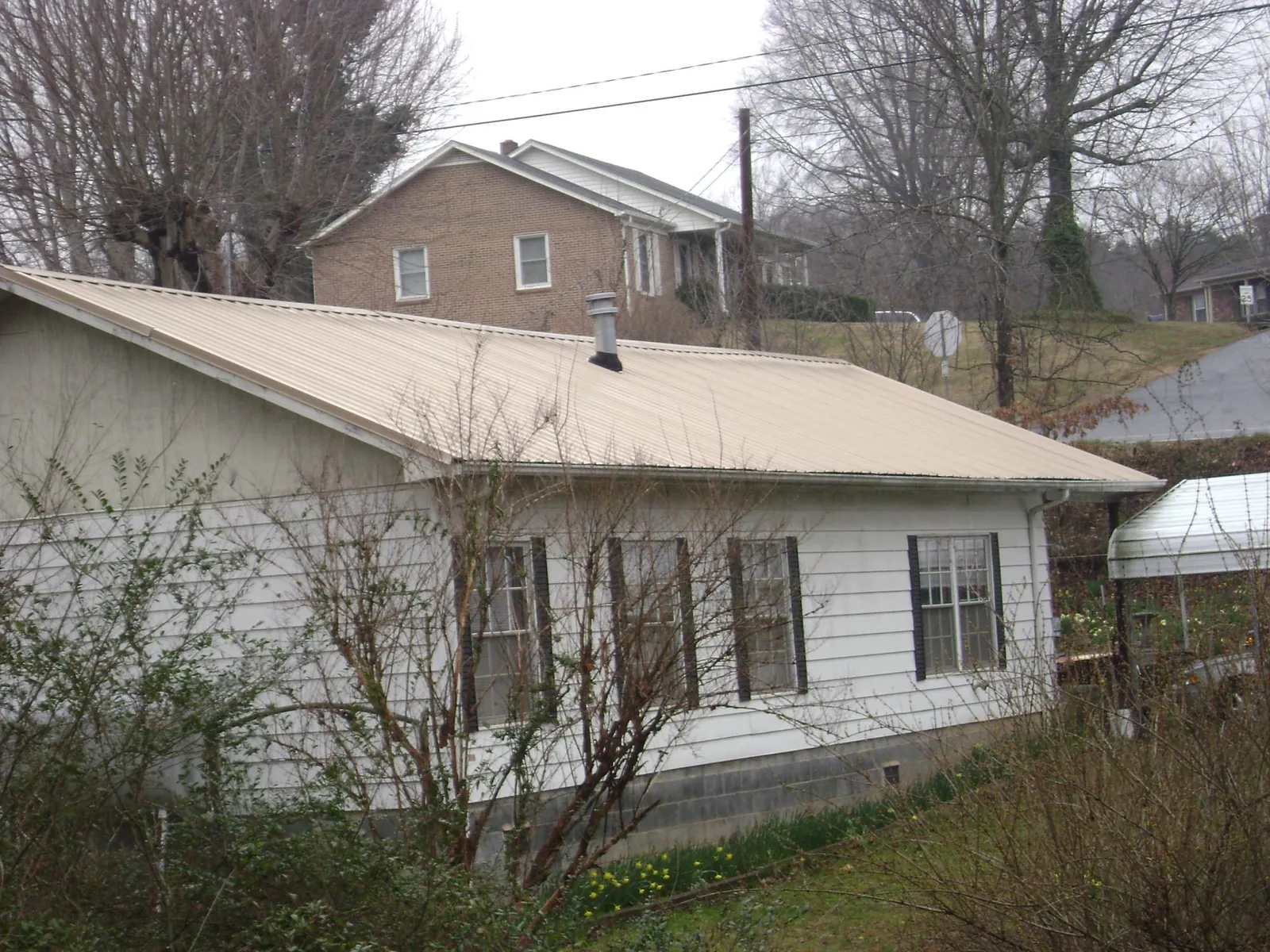 Tan metal roof on a white sided house set into a hillside — Commercial Roofing by Roofing Brothers in Burley